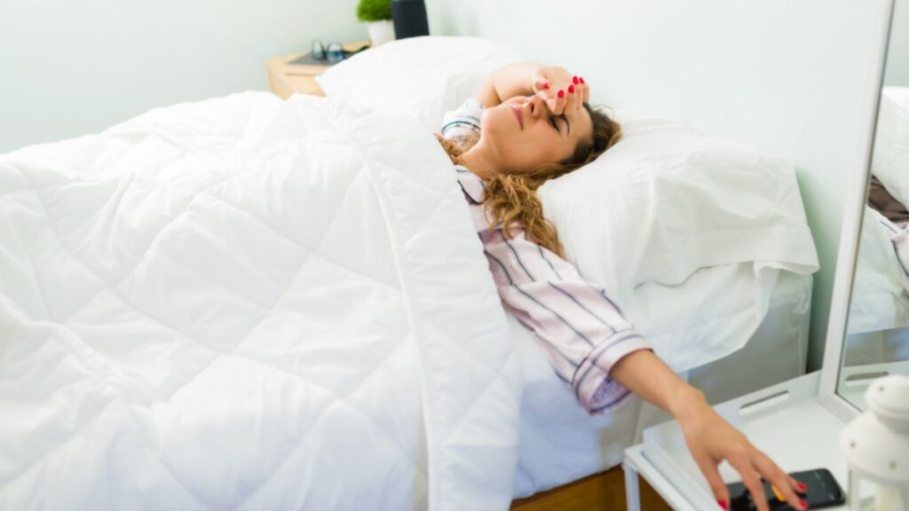 A woman lying in bed with her eyes closed, expressing reluctance to face the workday ahead.