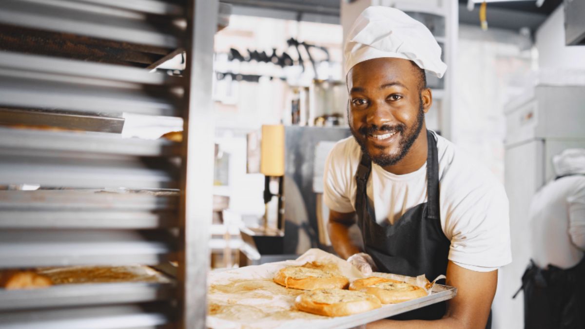 A cheerful man presents a tray of baked goods, reflecting his natural talent and the joy of meaningful work.