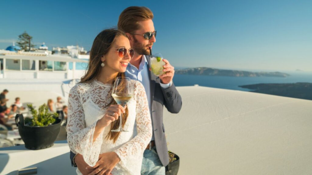 A man and woman enjoy wine on a rooftop, with a stunning ocean view, embodying a relaxed and luxurious lifestyle.