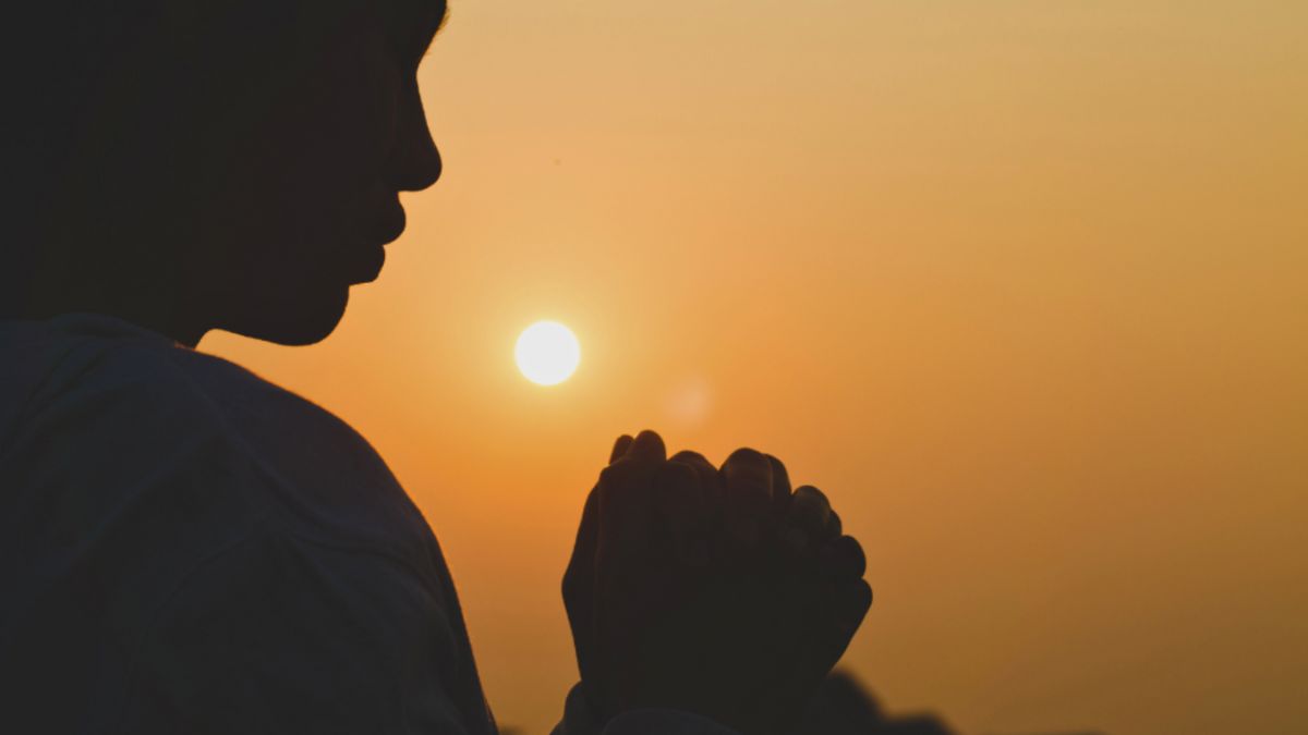 At sunset, a silhouette of a woman praying, embodying faith and the journey towards a good life.